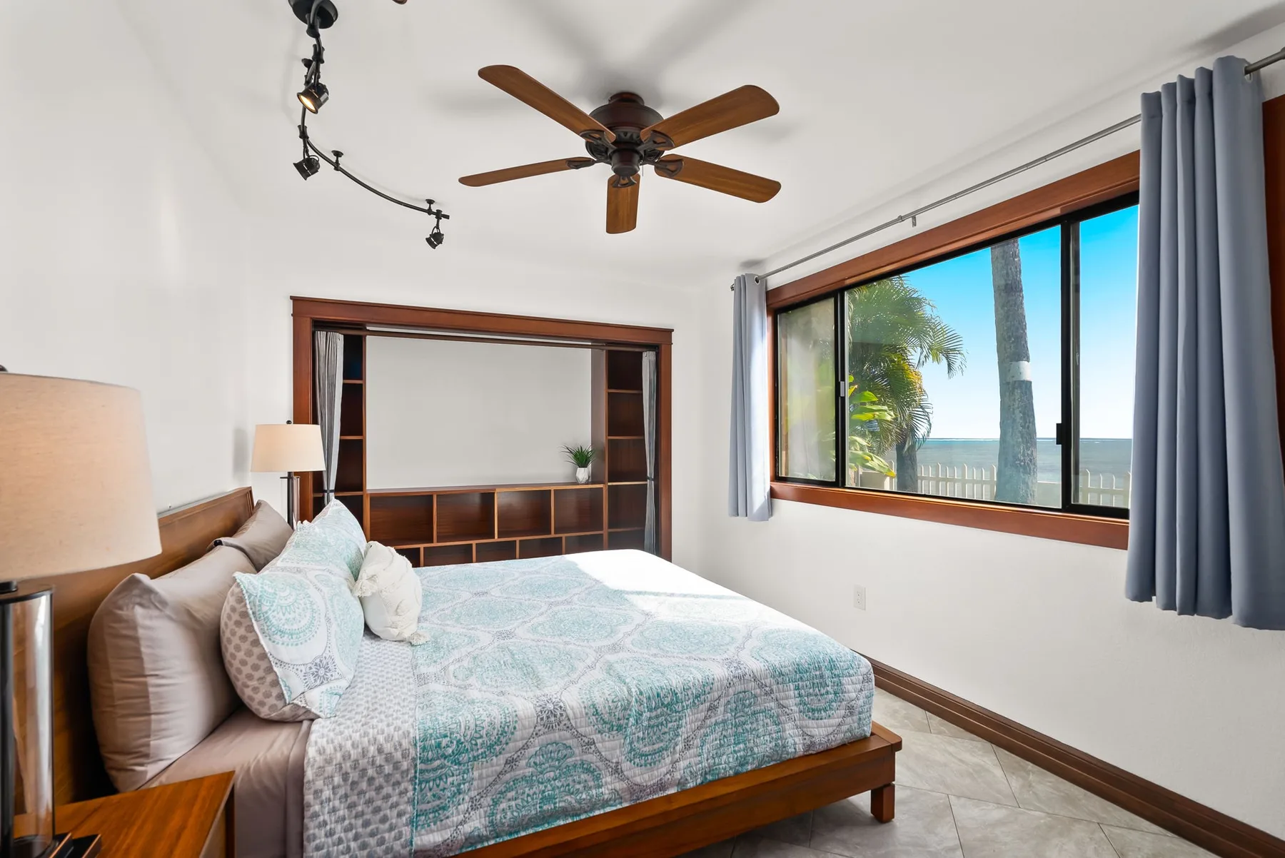A bedroom with a bed, ceiling fan, and a large window overlooking the water.