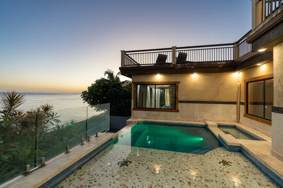 A pool beside a seaside building, with a glass railing and balcony.