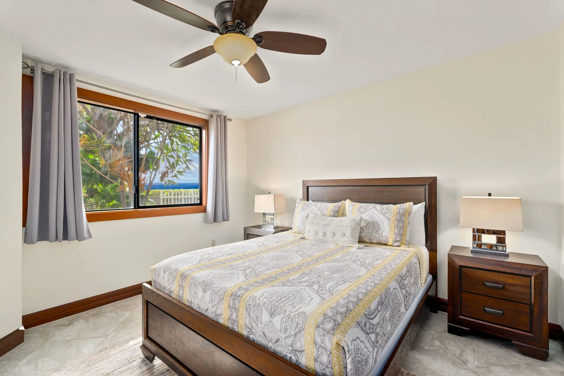 A bedroom with a bed, bedside tables, and a window overlooking greenery.