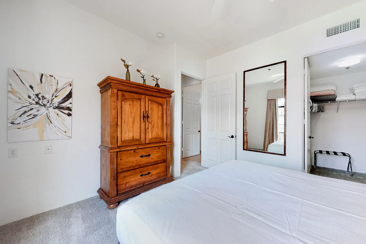 Un dormitorio luminoso con una cama blanca, un mueble de madera y un espejo de pared.