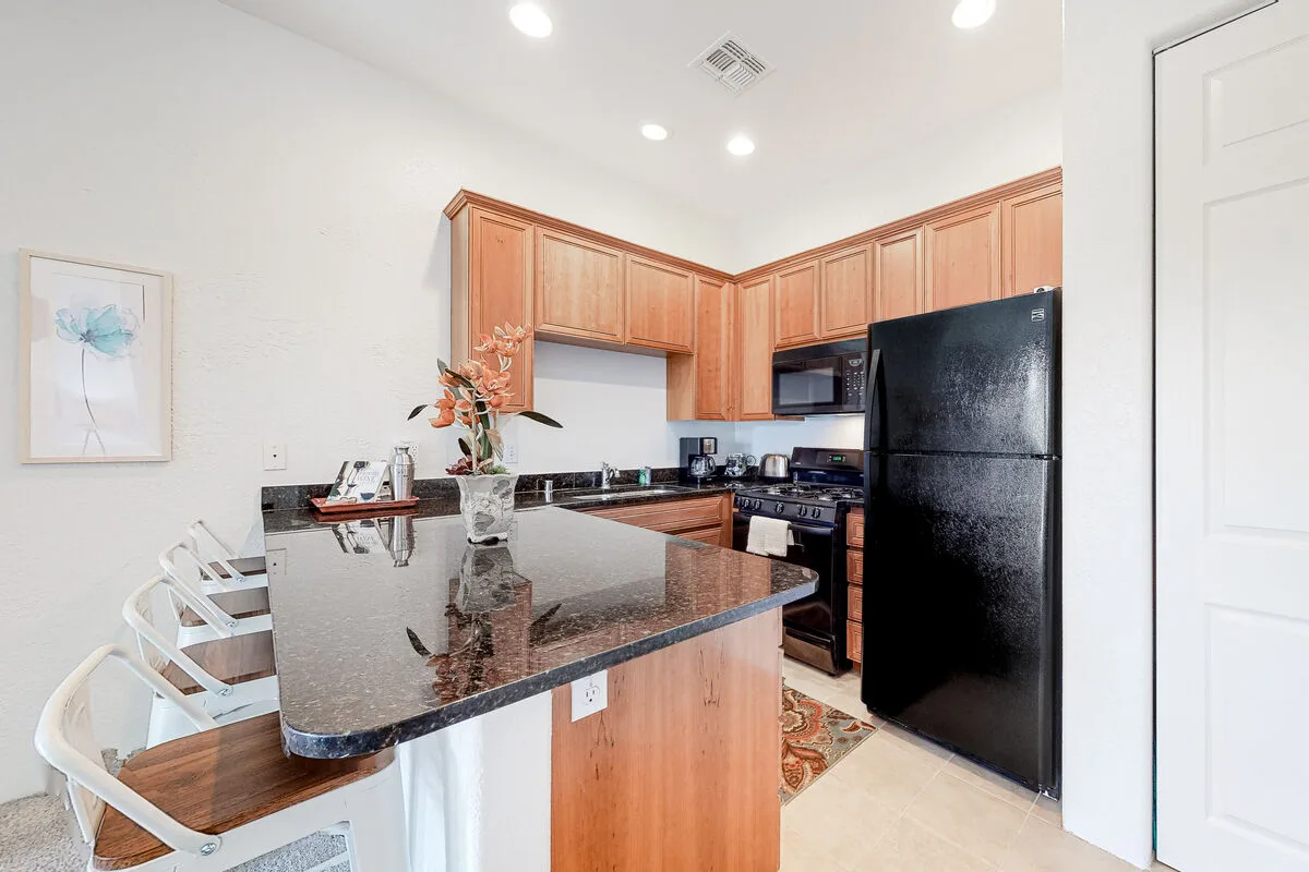 Una cocina con gabinetes de madera, un refrigerador oscuro y una barra con asientos.