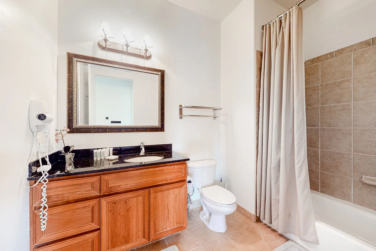 Un baño con mueble de madera, espejo, inodoro y ducha con cortina.