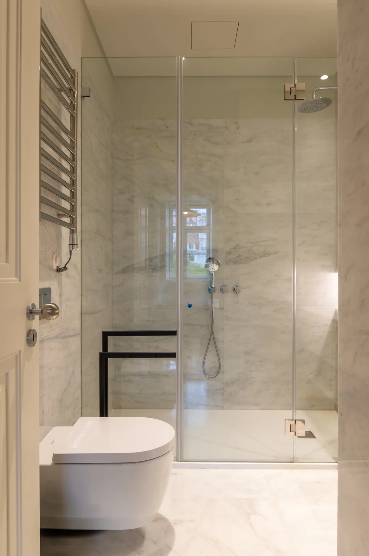 A bright bathroom with a glass shower and a wall-mounted toilet.