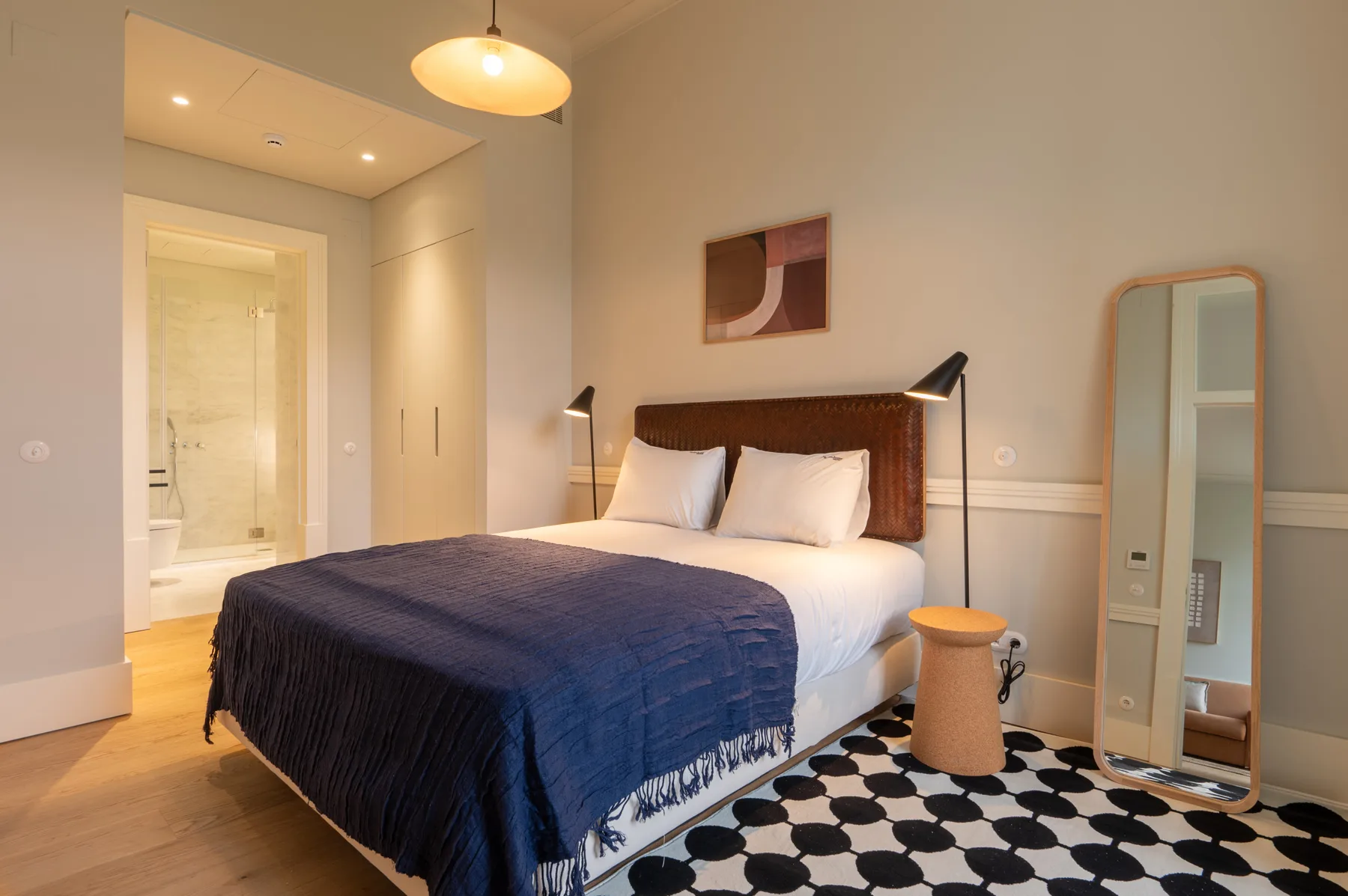 A bedroom with a bed covered by a dark blue blanket and a patterned rug.