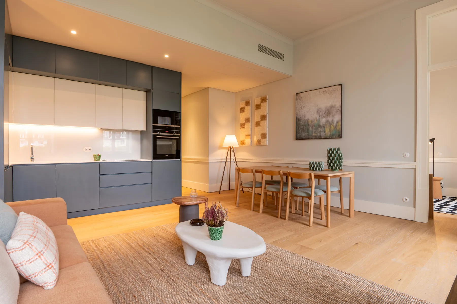 A bright open-plan living and dining area with a compact kitchen and wooden table.