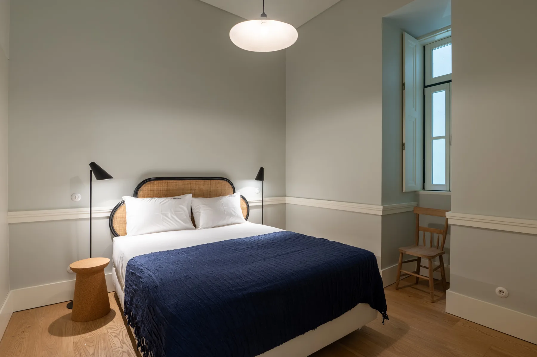 A bedroom with a bed, navy blanket, and a window beside a small chair.