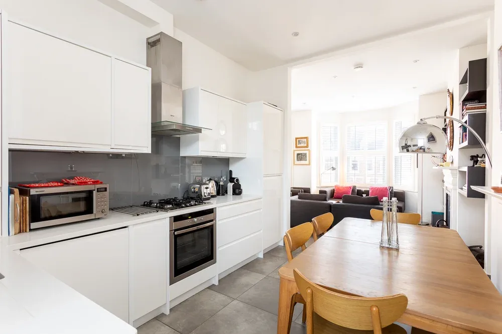 A bright open-plan kitchen and dining area with white cabinetry and a wooden table.
