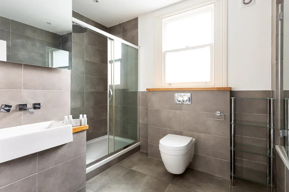 A tiled bathroom with a glass shower, wall-mounted toilet, and sink.