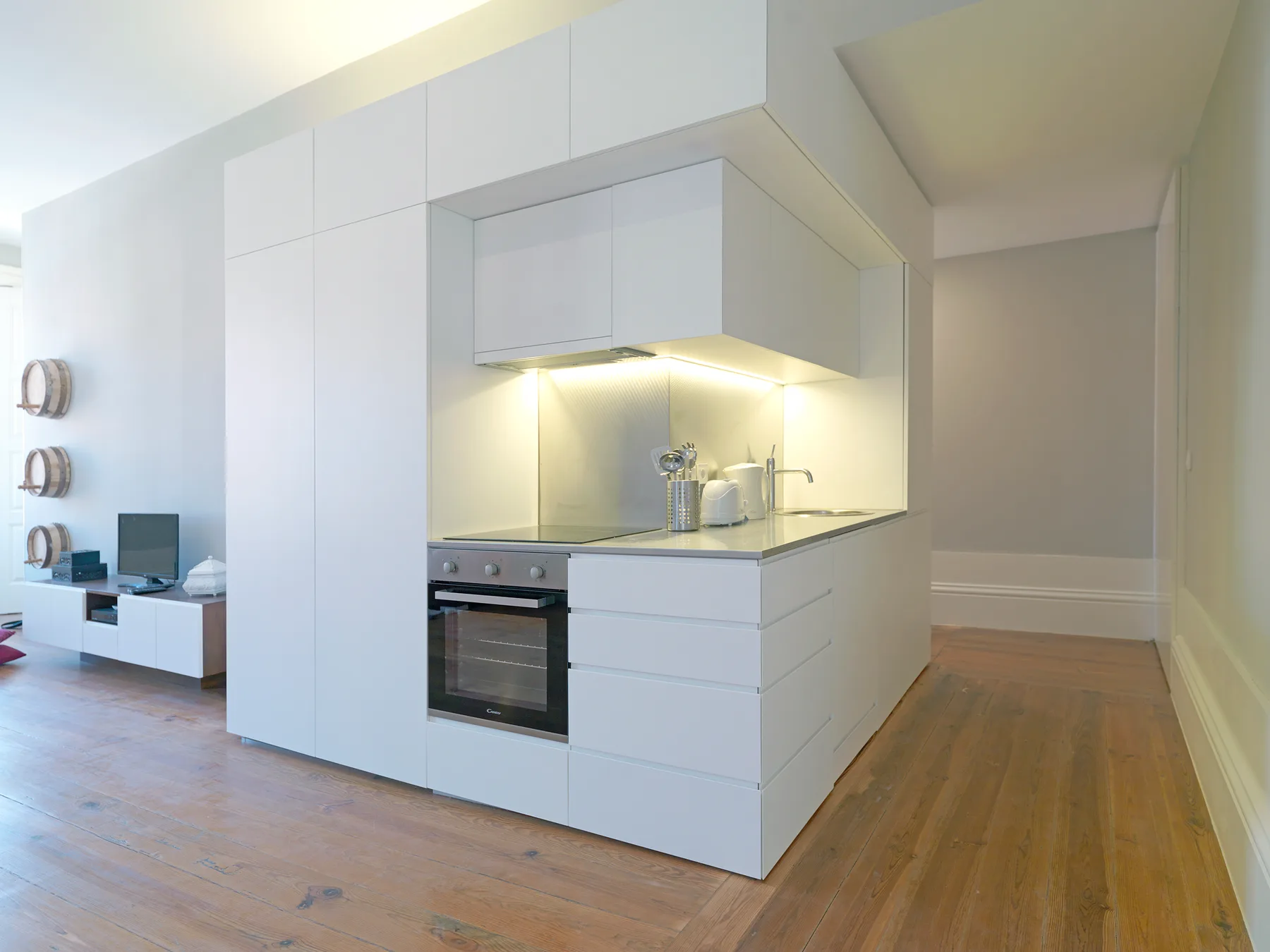 A bright modern kitchen with white cabinets, an oven, and wooden flooring.