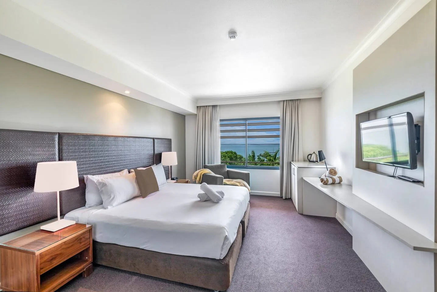 Un dormitorio luminoso con cama, zona de estar y televisor.