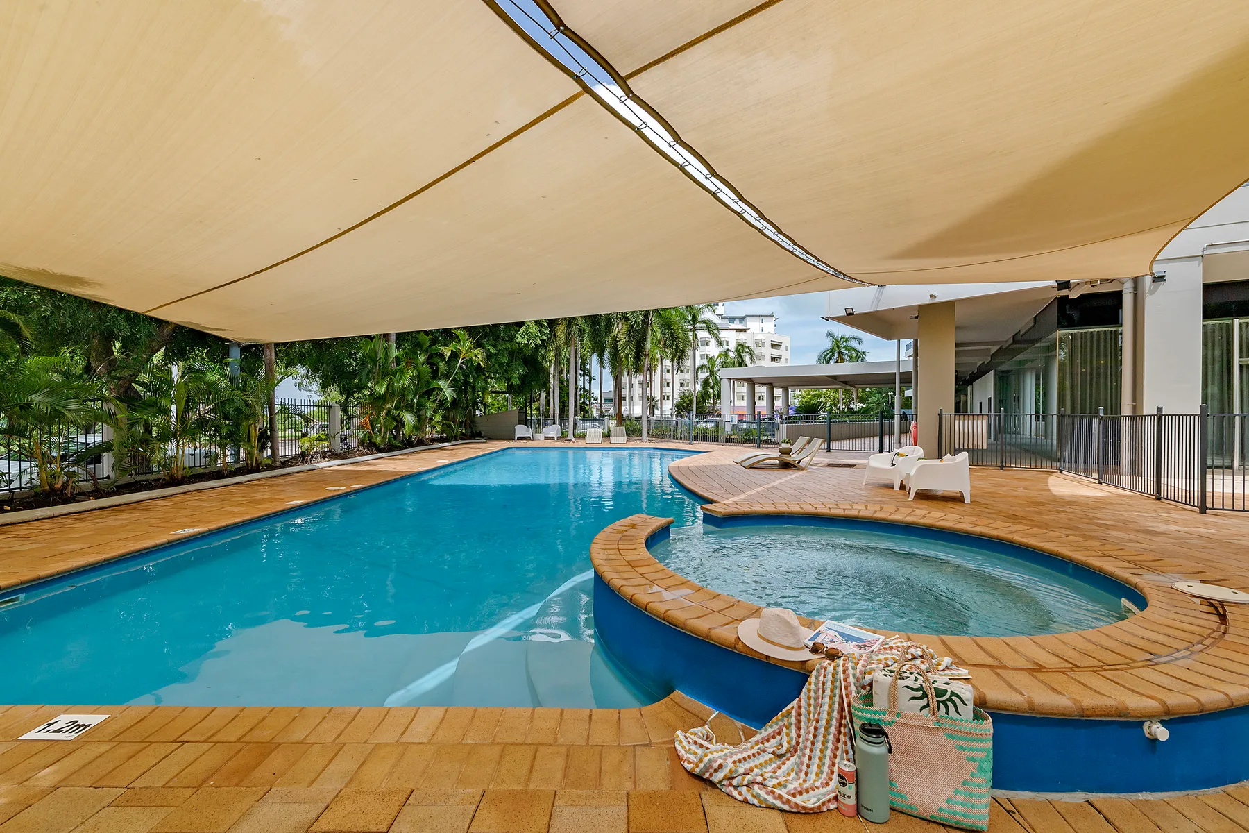 Una piscina al aire libre y un jacuzzi circular están bajo una gran cubierta de sombra.