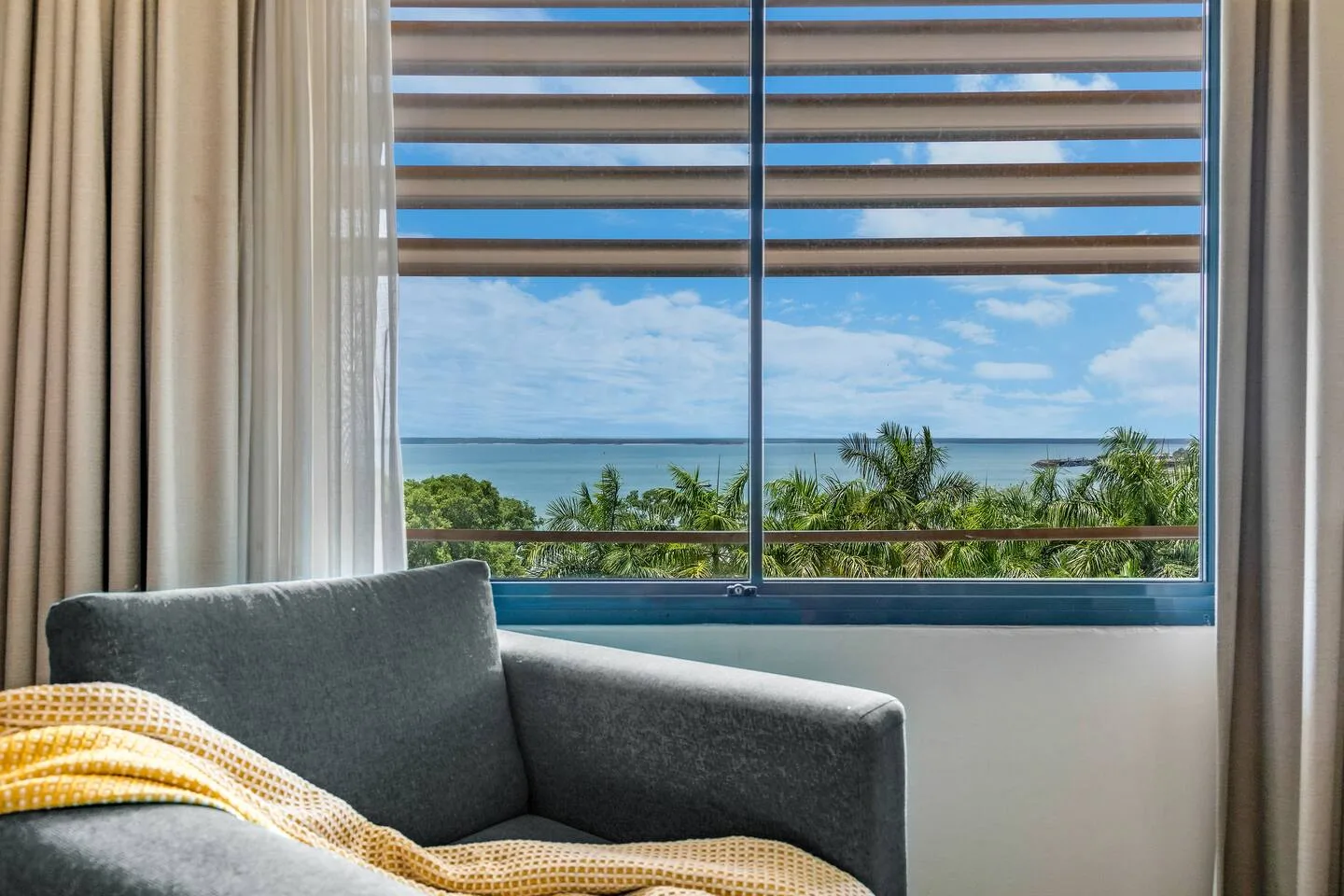 A seating area faces a large window overlooking the ocean and palm trees.