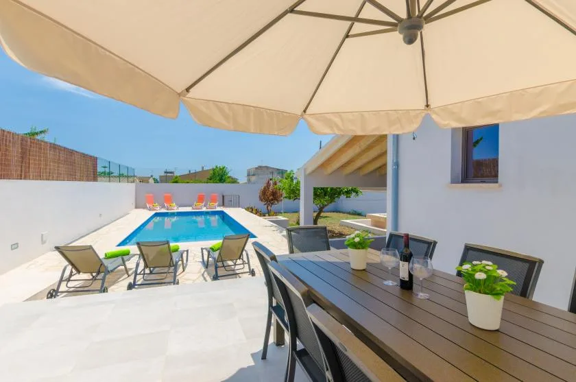 An outdoor dining area beside a swimming pool, shaded by a large umbrella.