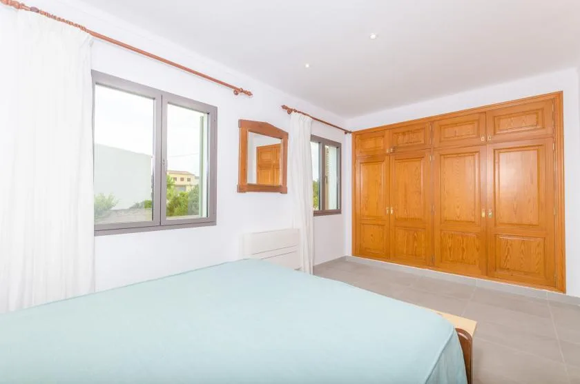 A bedroom with a bed, windows, and a large wooden wardrobe.