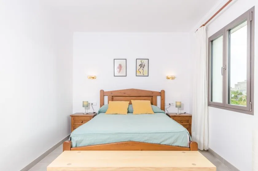 A bright bedroom with a wooden bed, bedside tables, and a large window.