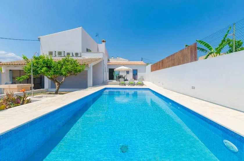 A swimming pool extends along a paved outdoor patio beside a modern building.
