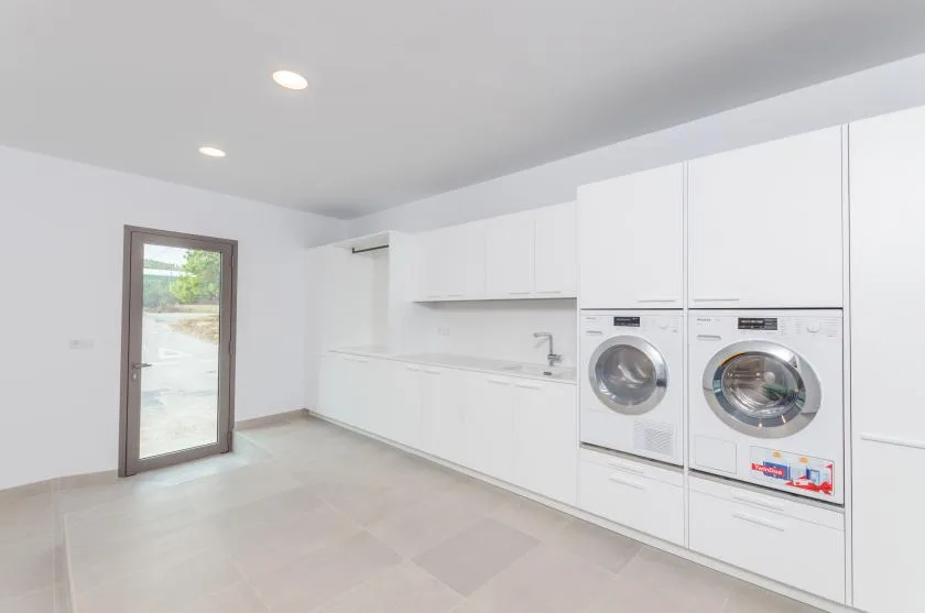 A bright laundry room with front-loading washing machines and white cabinets.