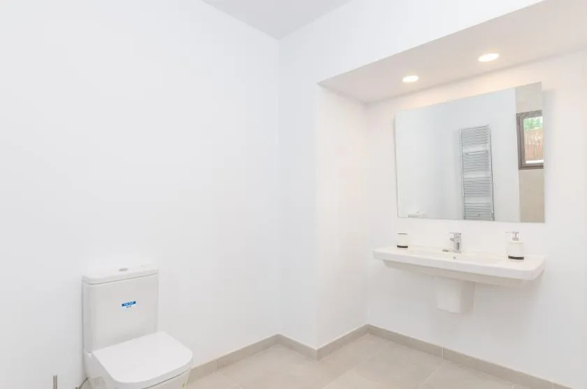 A bright bathroom with a toilet and a wide wall mirror above the sink.