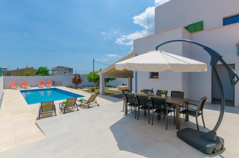 A sunny outdoor patio with a dining table, umbrella, and swimming pool.