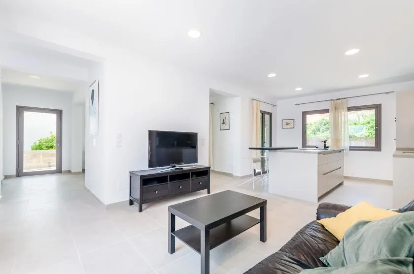 A bright open-plan living area with a television, coffee table, and kitchen island.