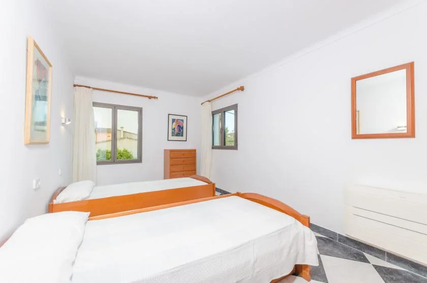 A bright bedroom with two beds, windows, and a dresser.