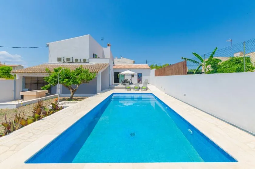 A rectangular outdoor pool extends toward a modern white house under a clear blue sky.
