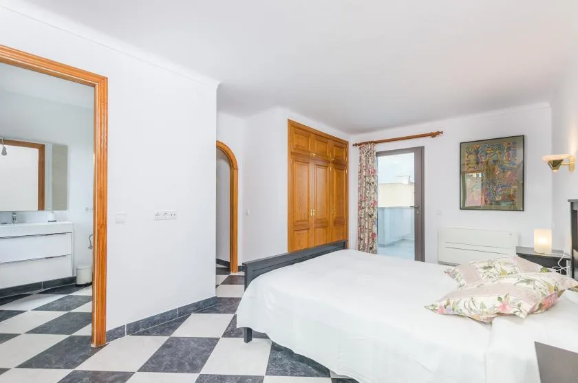 A bedroom with a bed, wooden doors, and a black-and-white tiled floor.