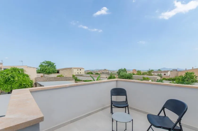 A rooftop terrace with seating overlooks nearby buildings beneath a blue sky.