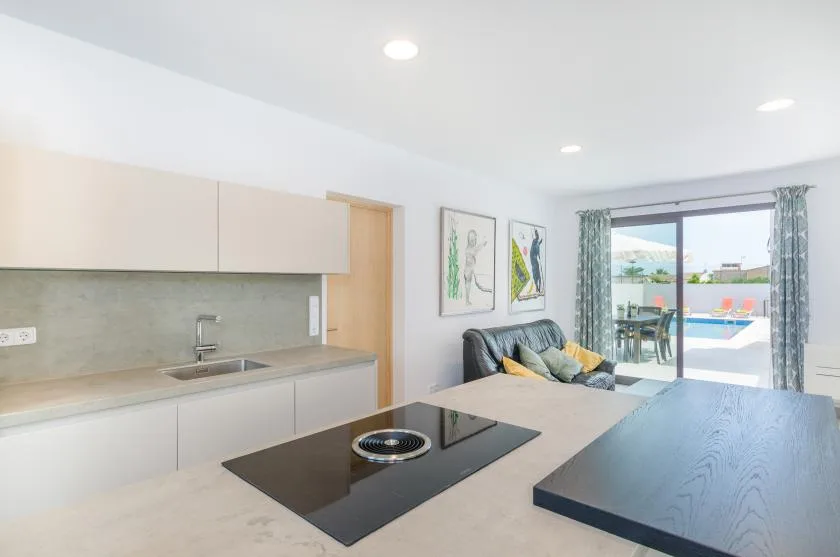 A modern kitchen with a countertop cooktop and a living area by glass doors.