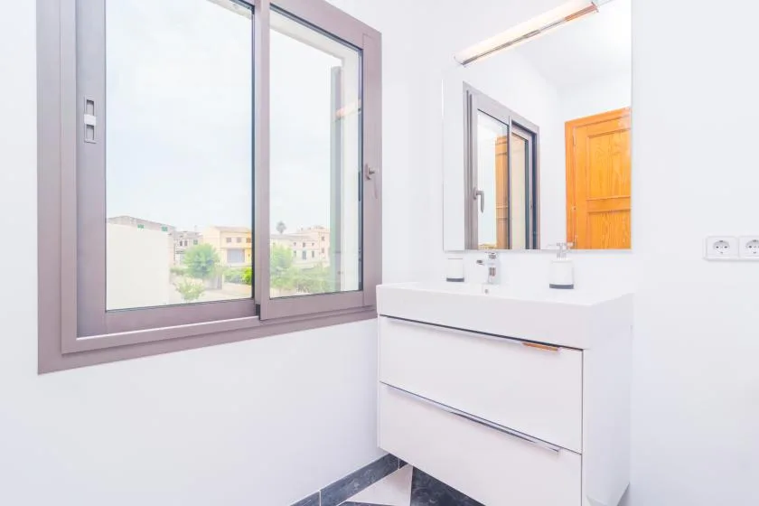 A bright bathroom with a wide window and a white vanity beneath a mirror.