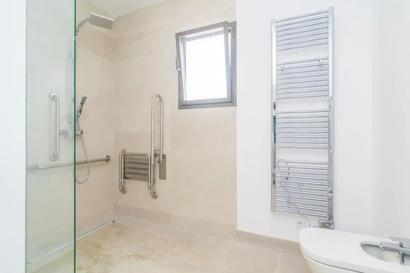 A bright bathroom with a glass shower, grab bars, and a wall-mounted towel warmer.