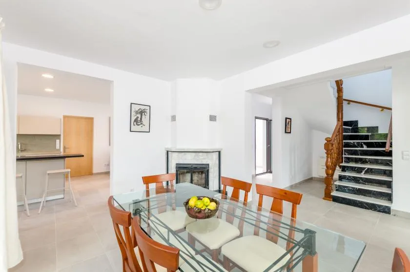 A dining area with a glass table, fireplace, and staircase.