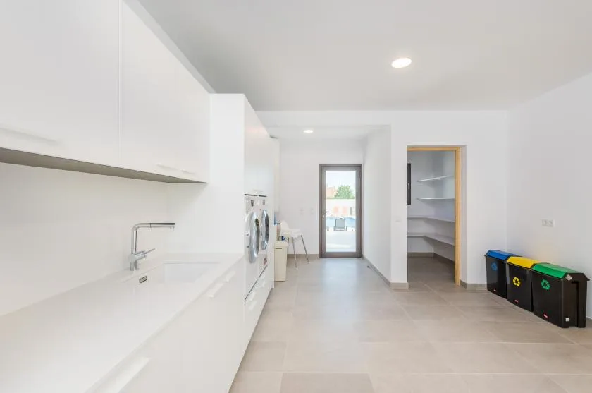 A bright utility room with a long white counter, laundry appliances, and open shelving.