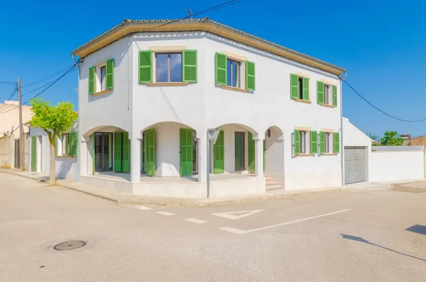A white corner building with green shutters and arched openings along the ground floor.