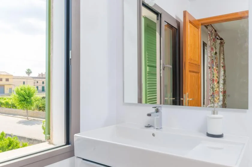A bathroom vanity and mirror sit beside an open window.