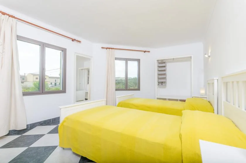 A bright bedroom with yellow bedding and large windows.