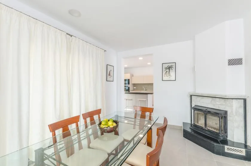 A bright dining area with a glass table and a fireplace.