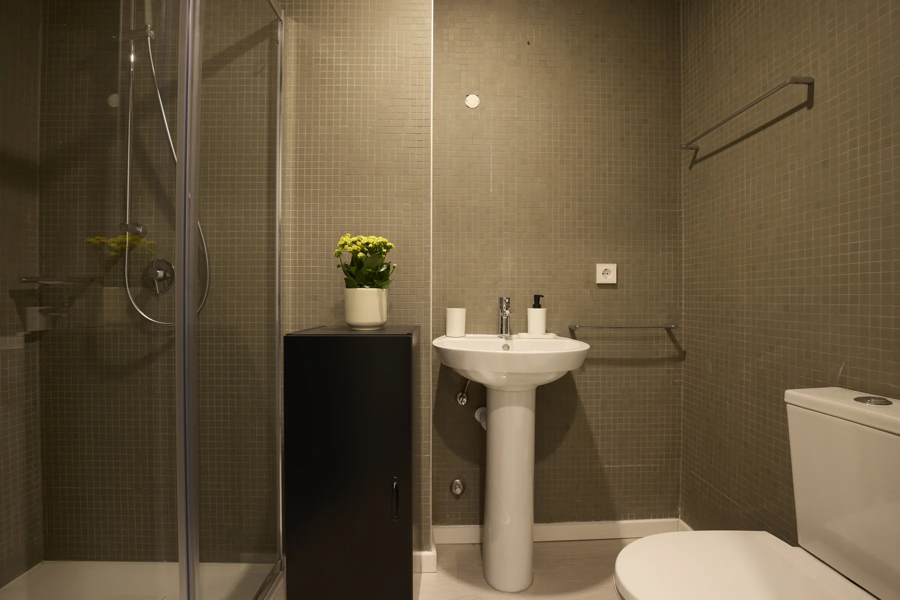 A tiled bathroom with a shower, pedestal sink, and toilet.