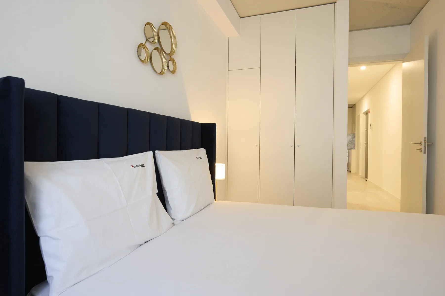 A bedroom with white bedding and a dark upholstered headboard.