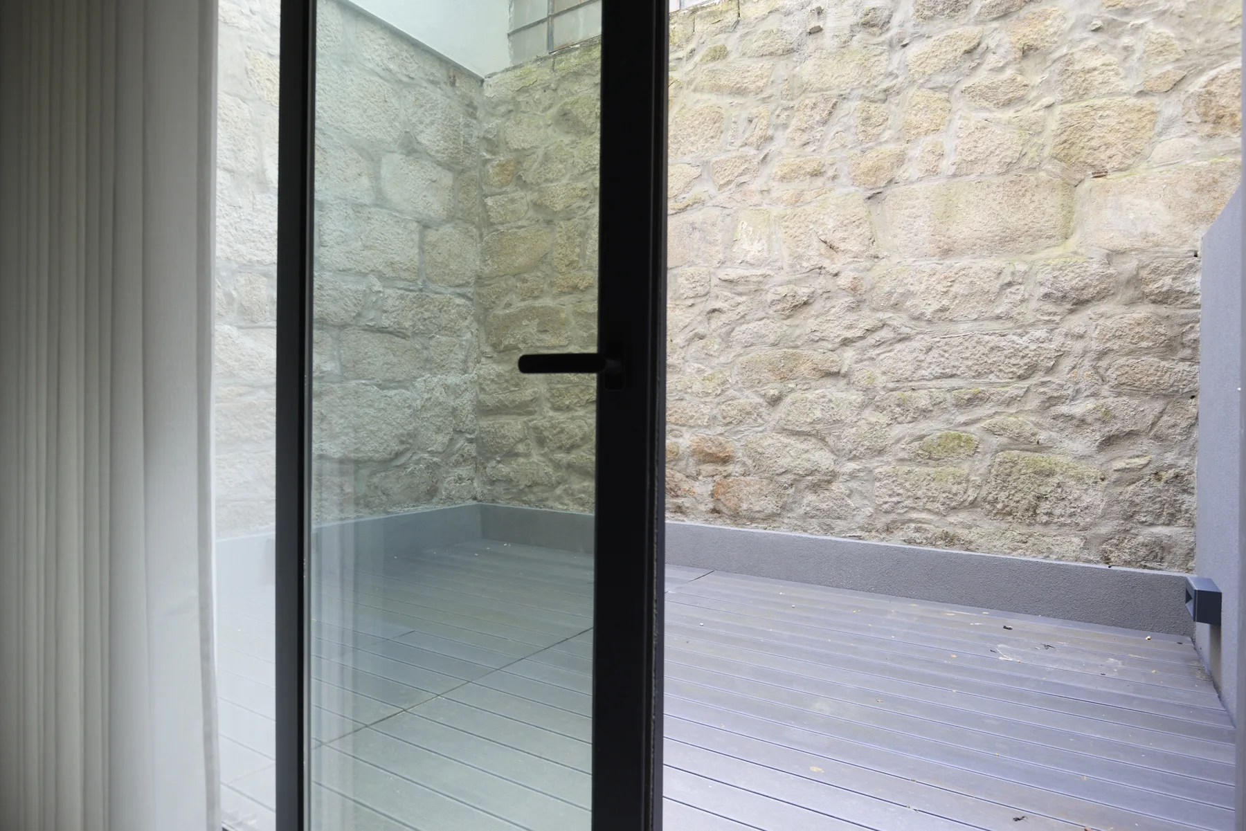 A small outdoor patio with gray decking beside a rough stone wall.