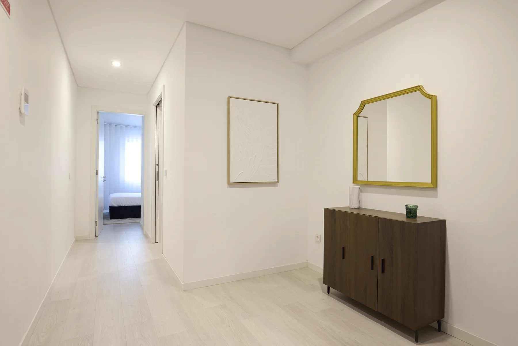 A bright hallway with a wooden cabinet and mirror beside an open doorway.