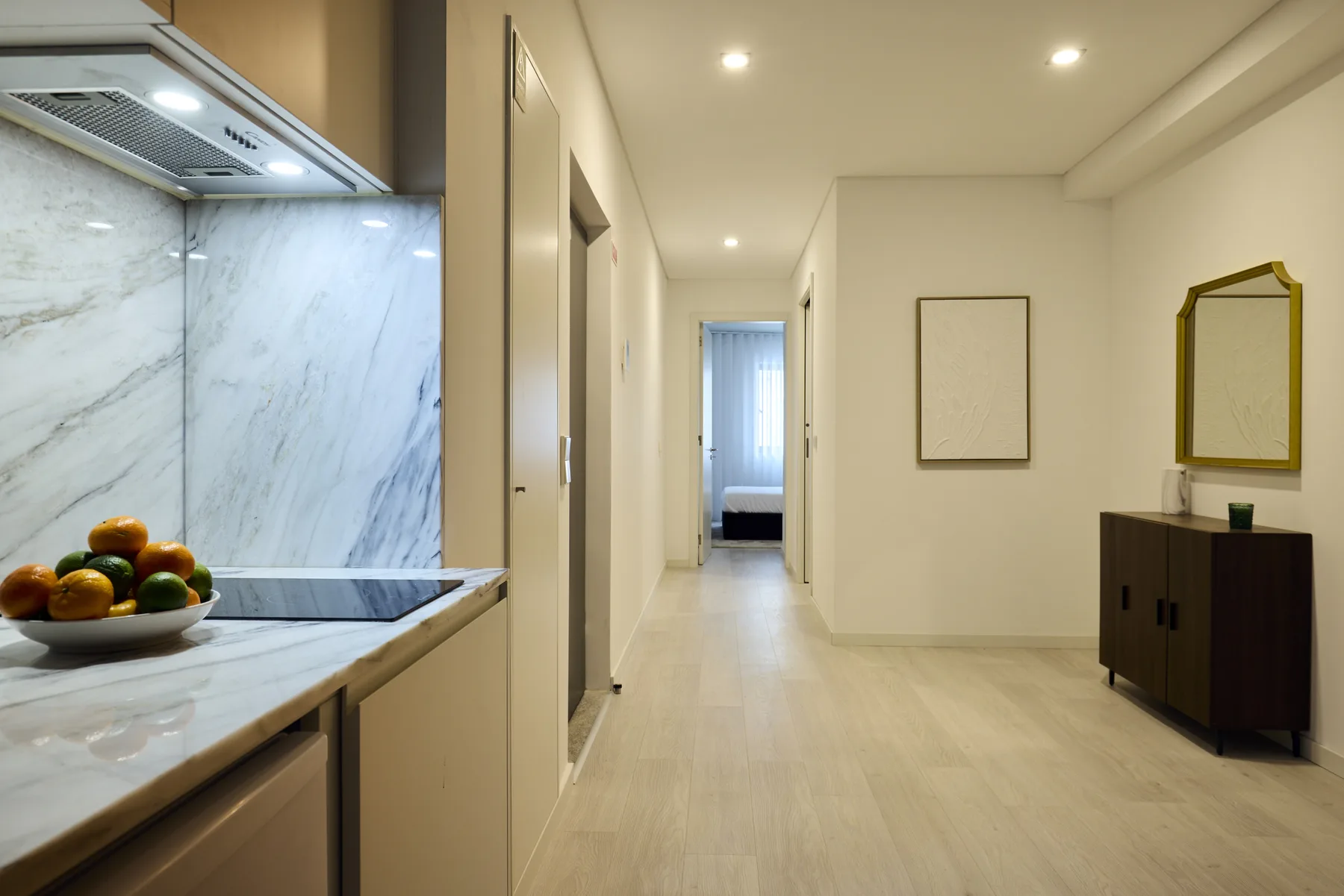A bright apartment hallway connects the kitchen area to a bedroom.