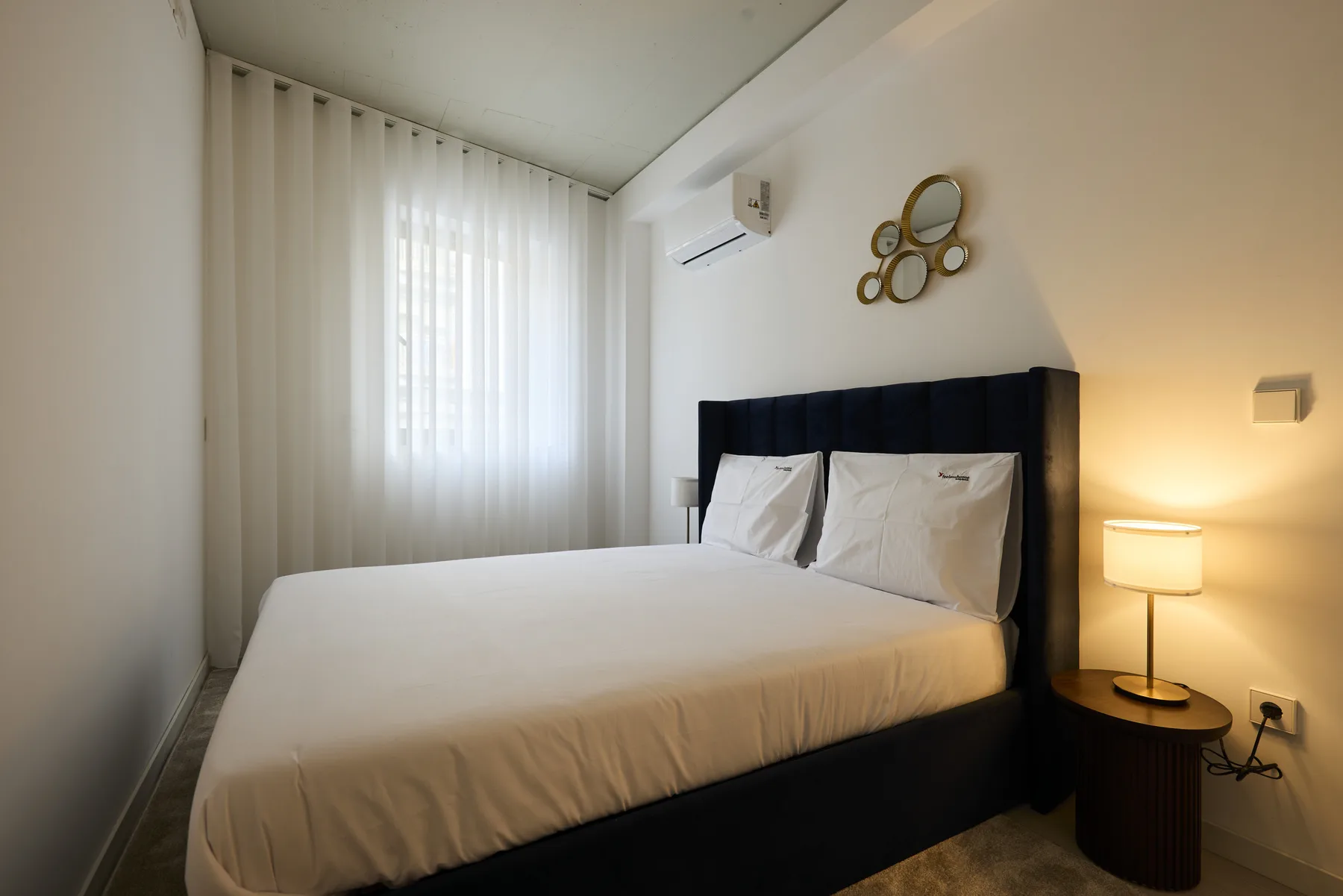A bedroom with a bed, sheer curtains, and a bedside lamp.