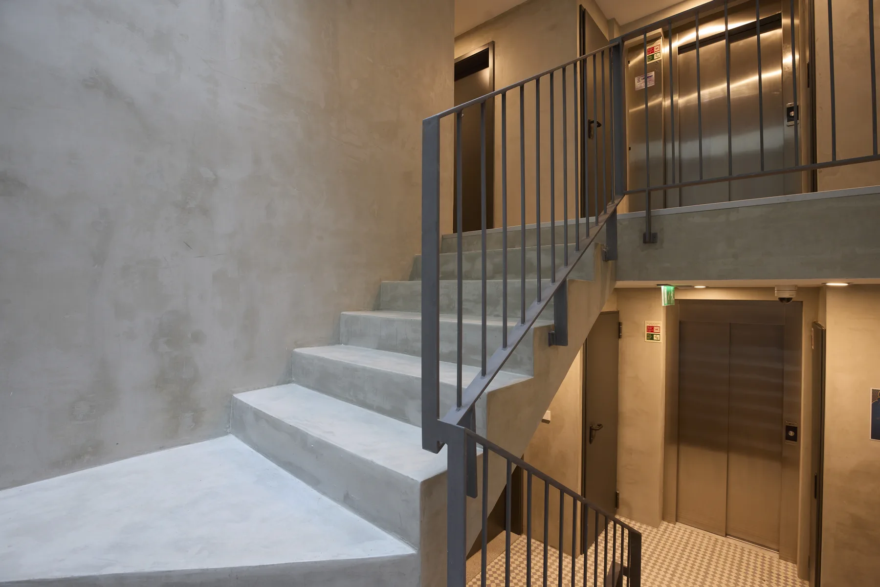 An indoor stairwell with concrete steps, metal railings, and an elevator.