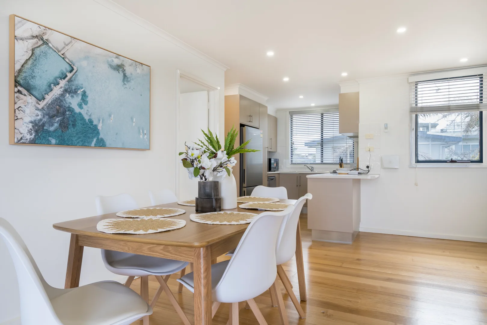 A dining area with a wooden table and white seating opens onto the kitchen.