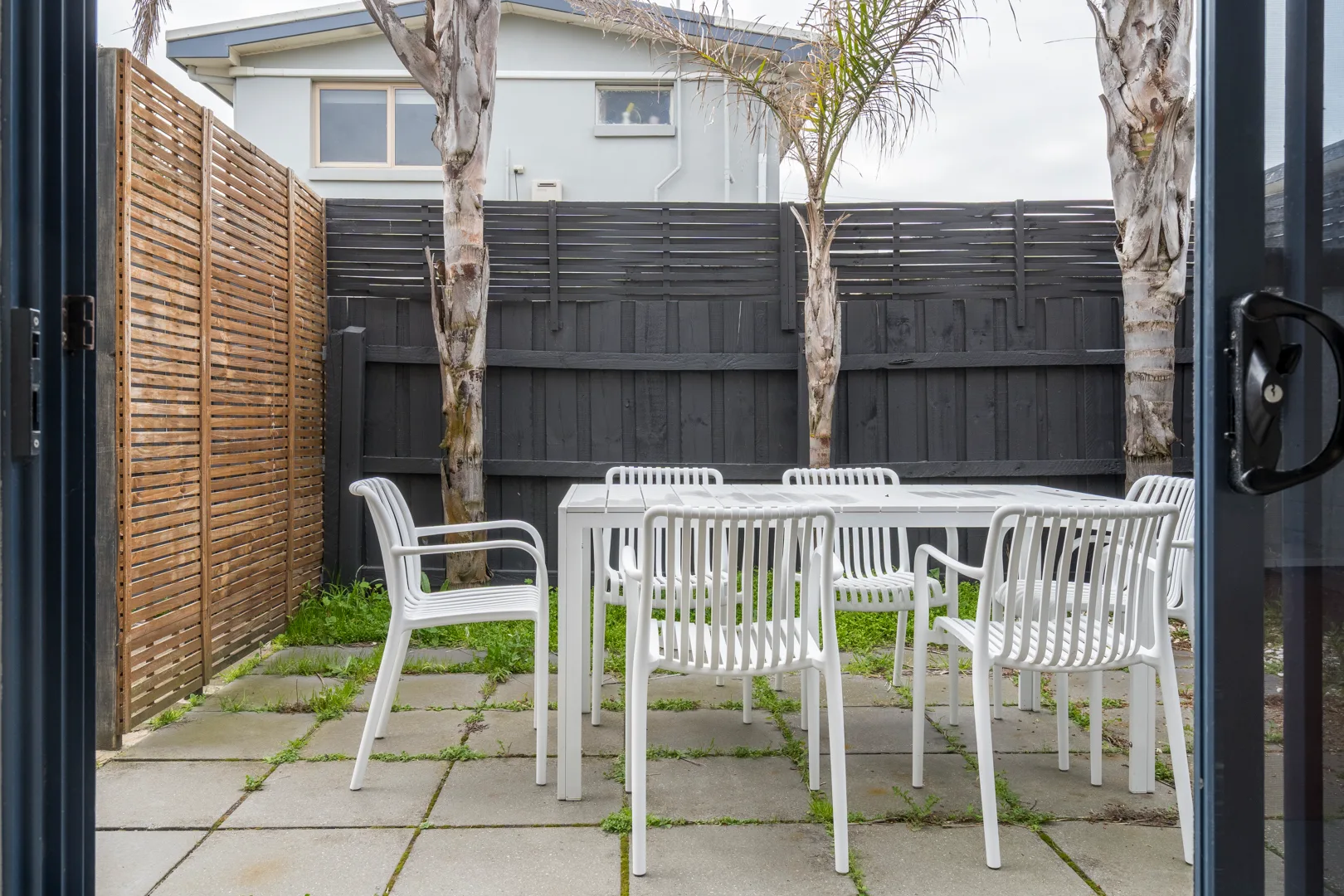 Una zona de comedor al aire libre tiene asientos blancos alrededor de una mesa en un patio pavimentado.