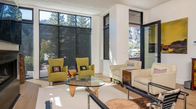 Una sala luminosa con grandes ventanas y asientos alrededor de una mesa de centro de vidrio.