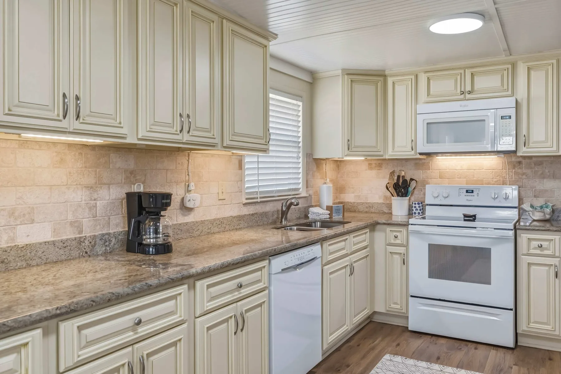 Una cocina luminosa con gabinetes claros, encimeras de piedra y electrodomésticos blancos.