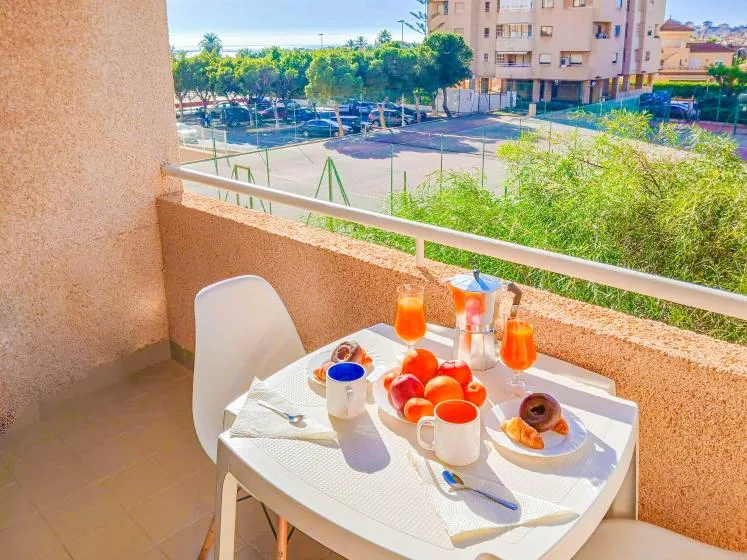 Una mesa de desayuno en un balcón da a una calle arbolada y edificios cercanos.