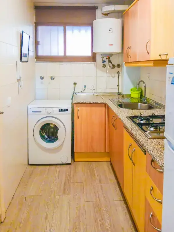 Una cocina estrecha con armarios de madera, fregadero y lavadora.